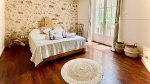 A bedroom with a stone-patterned wall, a wooden bed, a round woven rug, and a view through a glass door. - Charming 4* gite swimming pool and spa  (Le Fossat)