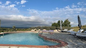 A swimming pool with a stone deck, surrounded by lounge chairs and umbrellas, with a view of the countryside. - Charming 4* gite swimming pool and spa  (Le Fossat)