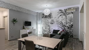 A modern dining area with a wooden table and chairs, a TV on the wall, and a tropical mural on the adjacent wall. - Cozy and renovated ground floor apartment connected (Roma)