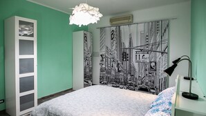 A bedroom with a bed, a wardrobe, a cityscape mural, a hanging light fixture, and a nightstand with a lamp. - Cozy and renovated ground floor apartment connected (Roma)