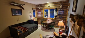 Una habitación acogedora con una cama, una mesa de comedor con sillas, una lámpara y varias decoraciones en la pared, incluyendo un pez, una cabeza de venado y un letrero que dice 'AIRPLANE HANGAR'.