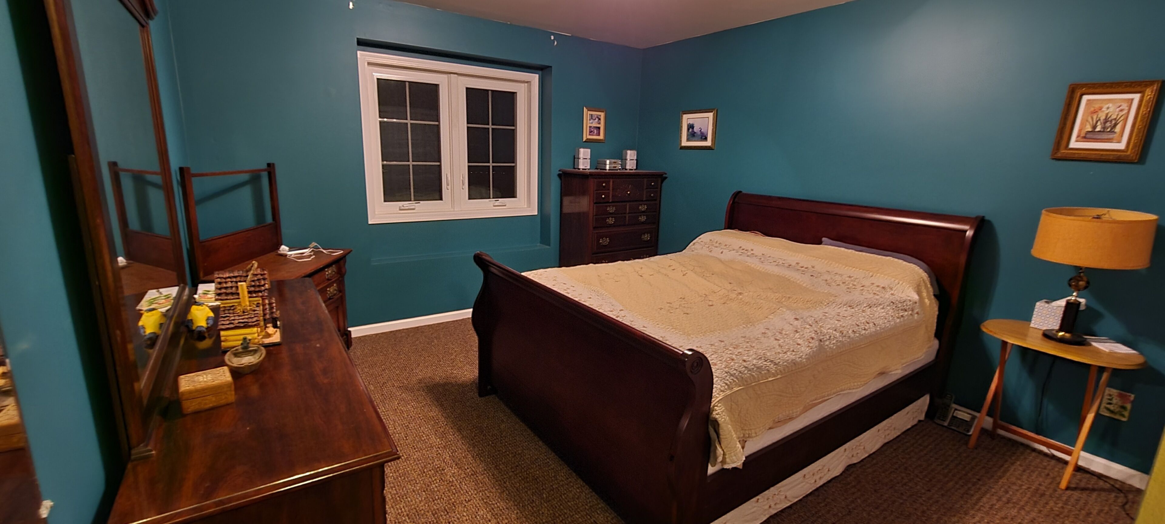 A bedroom with a bed, dresser, mirror, window, and a lamp.