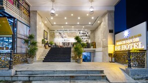 A modern hotel entrance with a staircase leading to the lobby, a large illuminated sign, and potted plants. - DB HOTEL (Nha Trang)