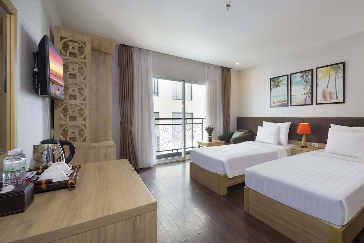 A hotel room with two beds, a desk, a TV, and a balcony with a view.