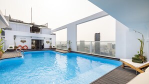 An indoor swimming pool with a wooden deck, lounge chairs, and potted plants. - DB HOTEL (Nha Trang)