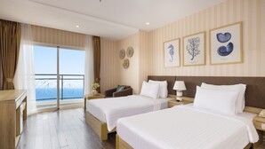 A hotel room with two beds, a desk, a chair, and a view of the sea. - DB HOTEL (Nha Trang)