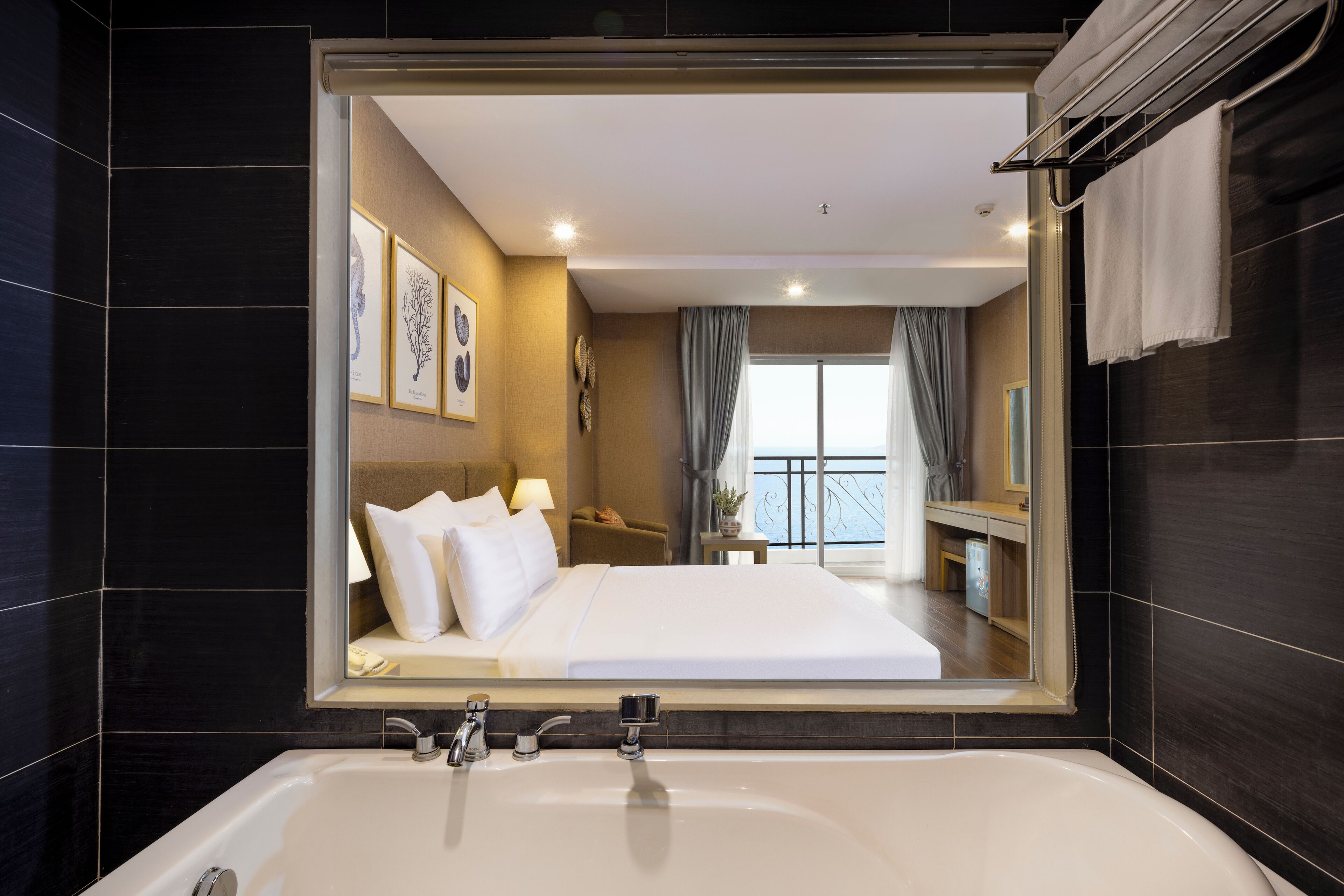 A modern hotel room with a large mirror, a white bathtub, and a bed with white linens.