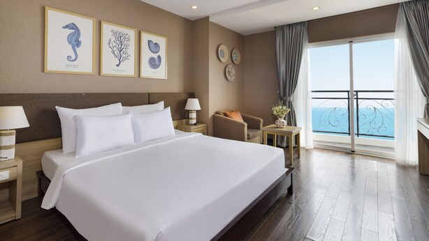 A spacious hotel room with a large bed, a nightstand, a chair, and a view of the sea through a balcony. - DB HOTEL (Nha Trang)