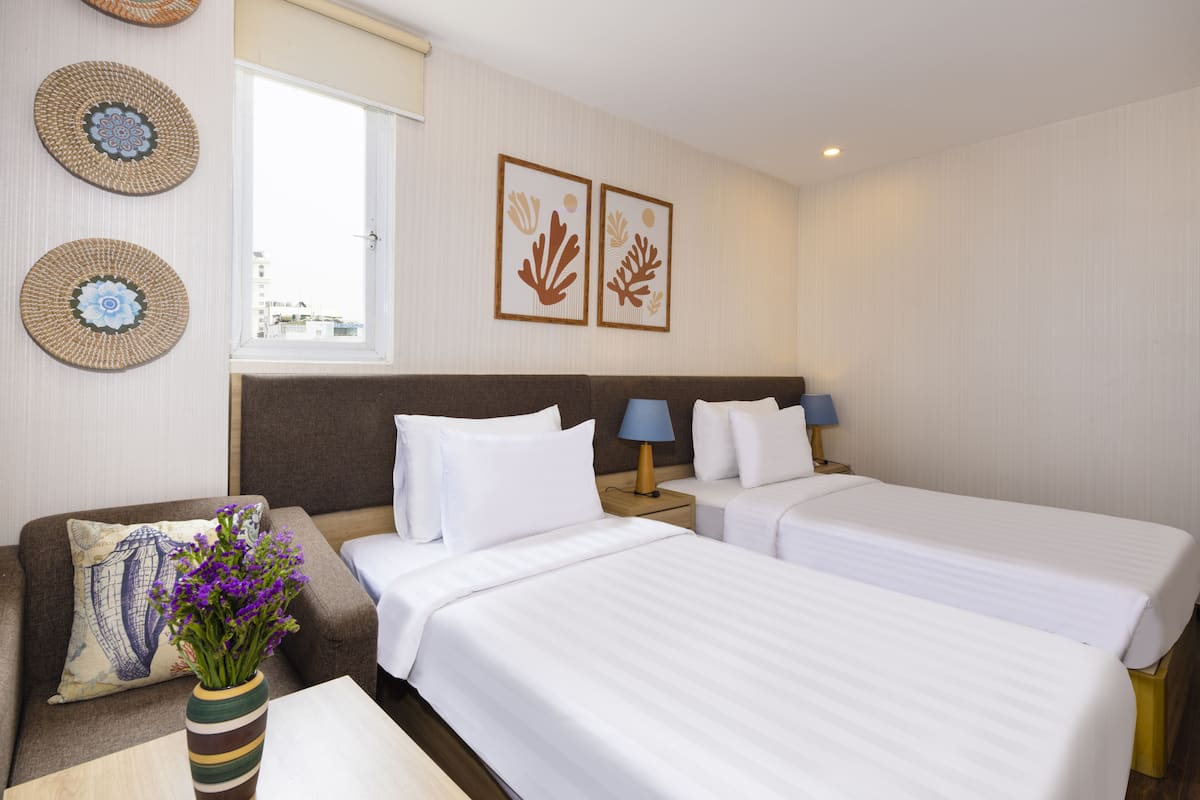 A hotel room with two beds, a wooden nightstand, a small table, and a window with blinds.