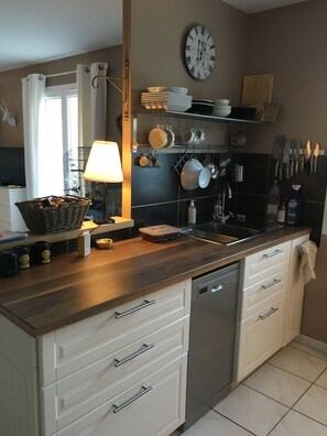 Een moderne keuken met een vaatwasser, witte kasten, een houten aanrecht en een klok aan de muur.