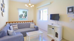 A living room with a sofa, a coffee table, a TV, and a window with a view of a pool. - Villa Kalithea in Nisaki (Corfu)