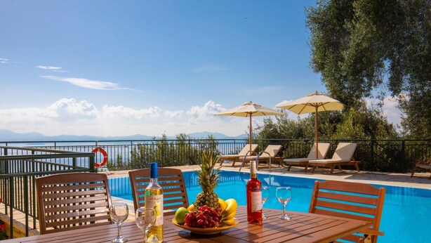 A poolside table with a bottle of wine, glasses, and fruit. - Villa Kalithea in Nisaki (Corfu)