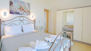 A bedroom with a bed, a painting, a wardrobe, and a bathroom visible through an open door. - Villa Kalithea in Nisaki (Corfu)