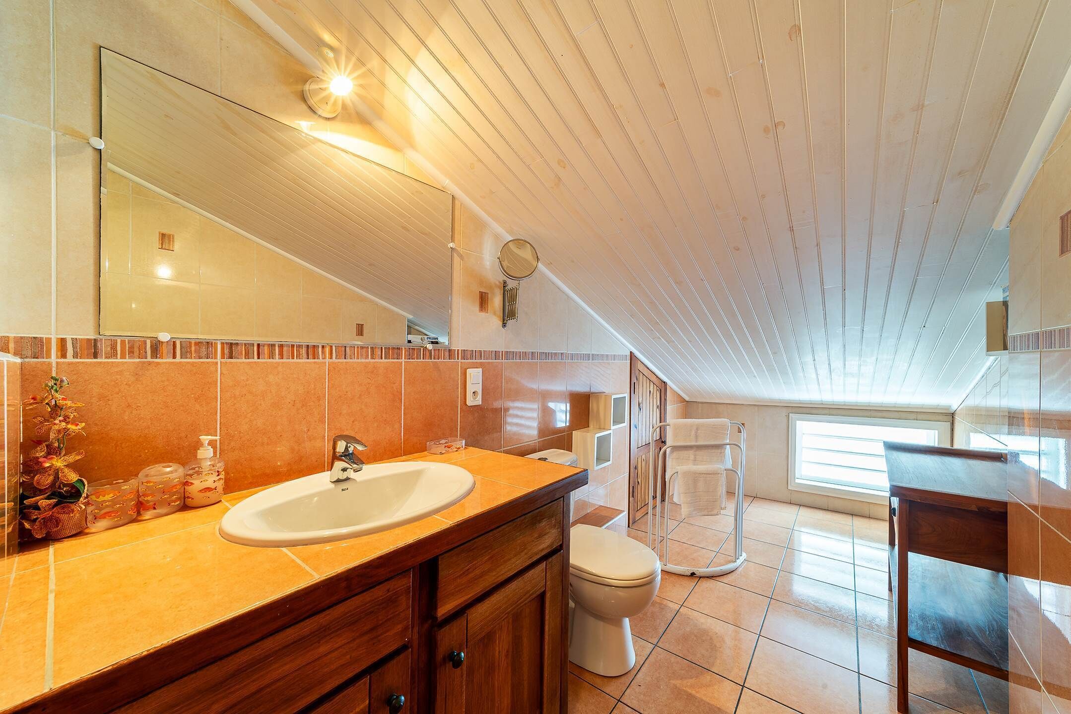 A modern bathroom with a large mirror, wooden vanity, and a toilet.