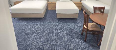 A hotel room with three beds, a small wooden table, and a blue carpet.