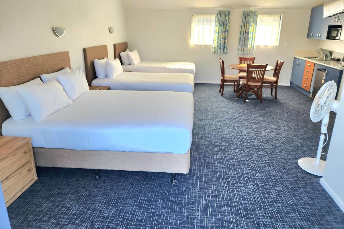 A hotel room with three beds, a dining table with chairs, a microwave, and a small kitchenette.