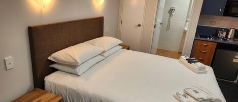 A hotel room with a bed, bedside table, and a small kitchenette.