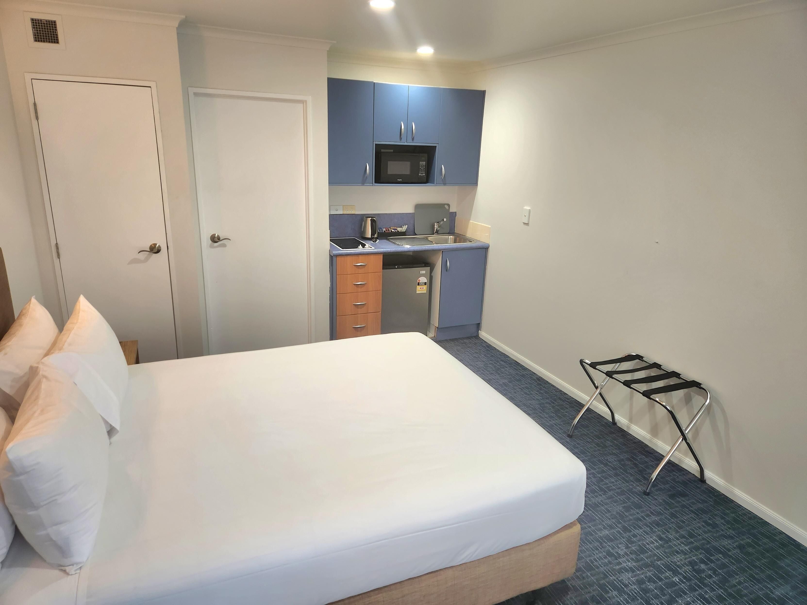 A compact hotel room with a bed, a small kitchenette, and a drying rack.