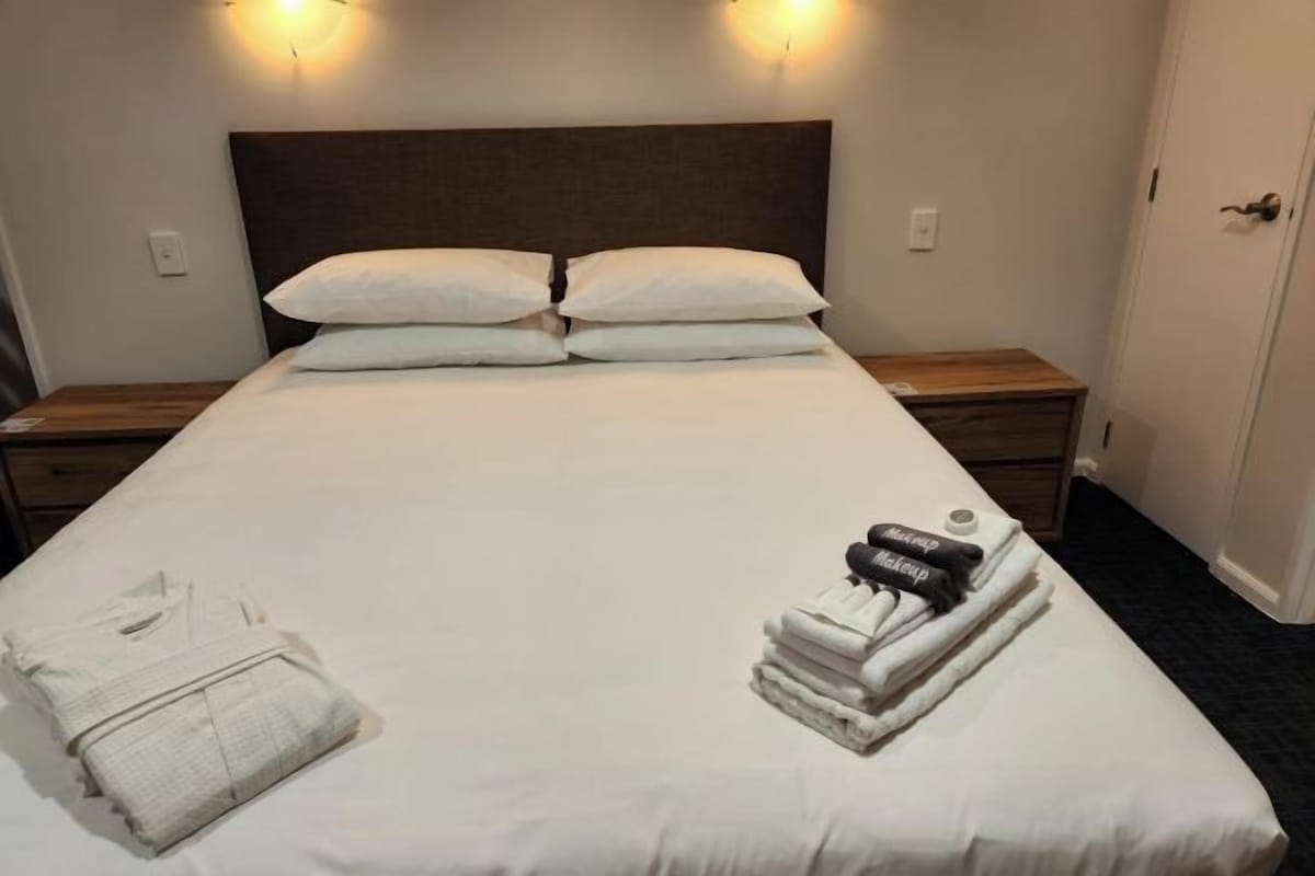 Una cama bien hecha con sábanas blancas, dos almohadas y una pila de toallas dobladas y una bata al lado.