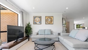 A modern living room with a sectional sofa, a glass coffee table, and a flat-screen TV. - Botany Palms Motel (Auckland)