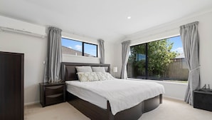 A modern bedroom with a large bed, a nightstand, a wardrobe, and a window with curtains. - Botany Palms Motel (Auckland)