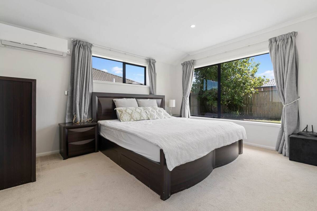 A modern bedroom with a large bed, a nightstand, a wardrobe, and a window with curtains.