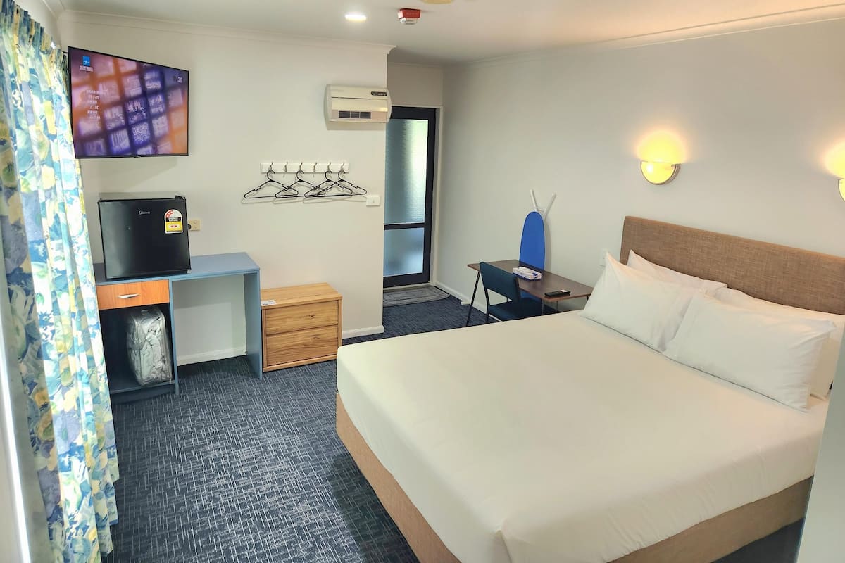 A hotel room with a bed, a desk, a television, a wall-mounted air conditioner, and a wall-mounted light fixture.