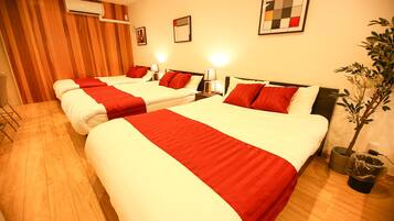 A hotel room with three beds, each with red and white bedding, a potted plant, and a wall-mounted air conditioner.