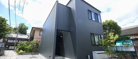 A modern two-story building with a unique angular design, a small garden area, and a visible outdoor space.