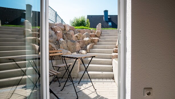 On voit un escalier en pierre menant à un patio où se trouvent une table et des chaises.