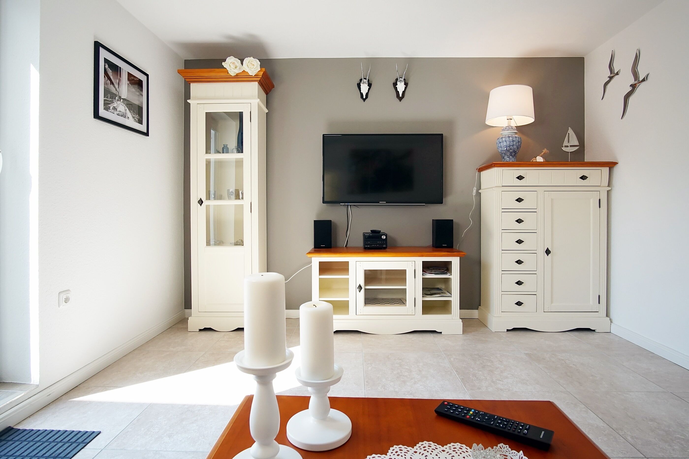 Ein Wohnzimmer mit Fernseher, weißen Schränken, einem Holztisch und einer Fernbedienung.