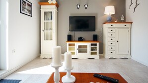 Un salon avec un téléviseur, des meubles blancs, une table en bois et une télécommande.