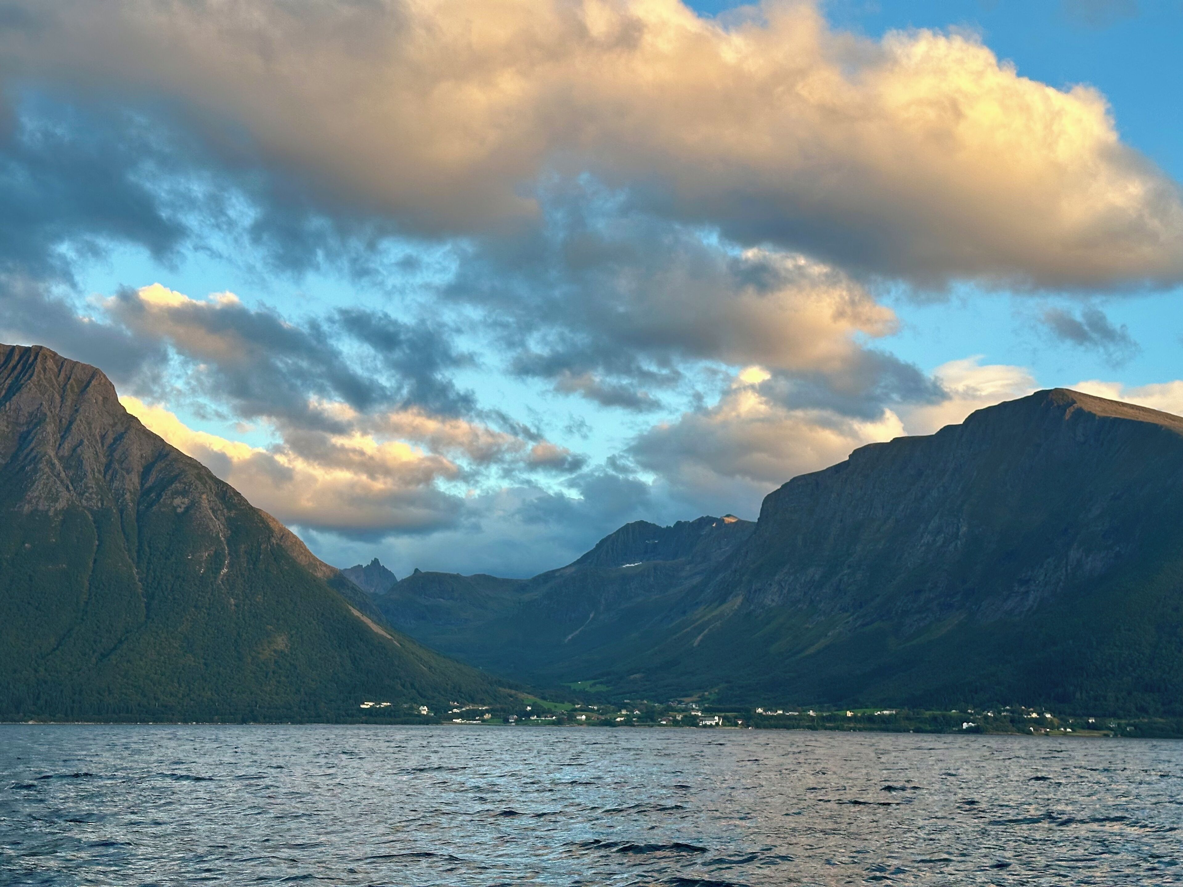 A mountainous landscape with a body of water in the foreground and a small settlement in the distance.