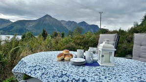 Ein Tisch ist mit Tellern, Tassen und einer Laterne gedeckt, mit Blick auf eine Berglandschaft.