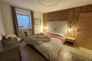 Una camera da letto con testiera in legno, un letto con coperta in pelliccia, un comodino, una finestra con tende e un termosifone.