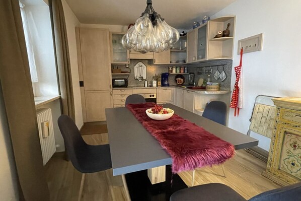 A modern kitchen with a dining table, chairs, a chandelier, and a red apron hanging on the wall. - Selva di Val Gardena, apartment for 6 close to the ski slopes (Selva di Val Gardena)