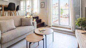 Een moderne woonkamer met een bank, twee bijzettafels en een eethoek met stoelen.