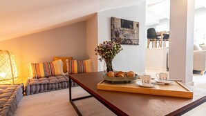Een moderne woonkamer met een bank, een bijzettafeltje met gebak en een vaas met bloemen.