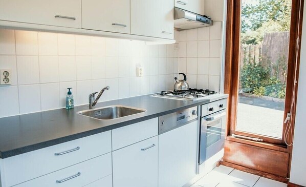 Een moderne keuken met witte kasten, een roestvrijstalen spoelbak, een gasfornuis en uitzicht op de omgeving via een glazen deur.