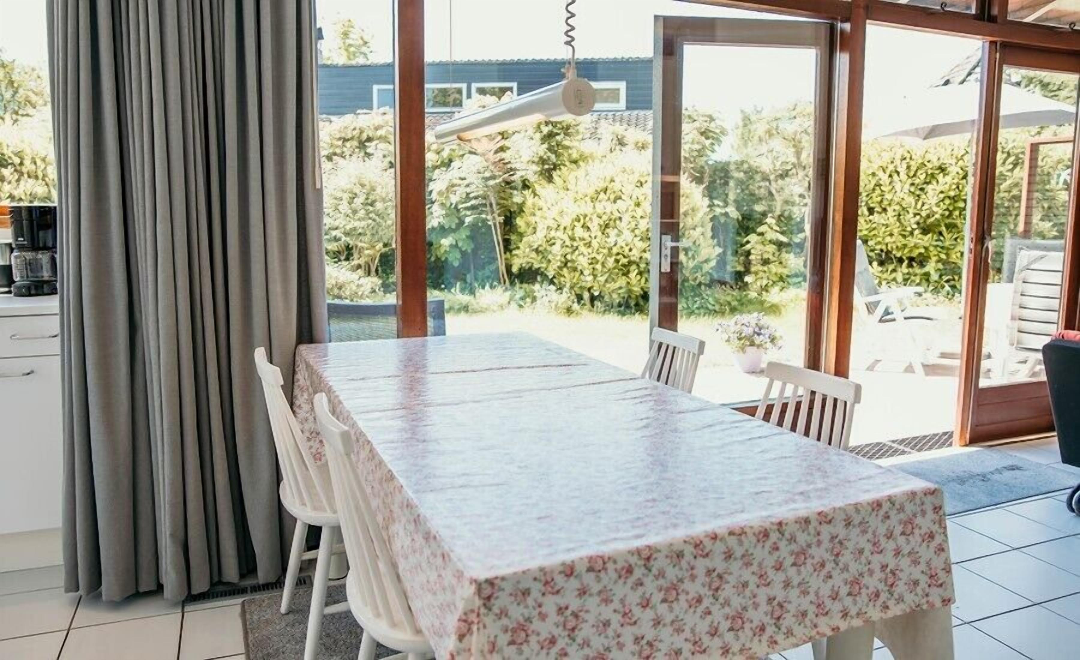 Un coin repas avec une table et des chaises, une fenêtre avec des rideaux et une vue sur la verdure à l’extérieur.