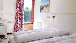 Un dormitorio con dos camas, una ventana con cortinas, una mesita de noche, una lámpara y un cuadro en la pared.