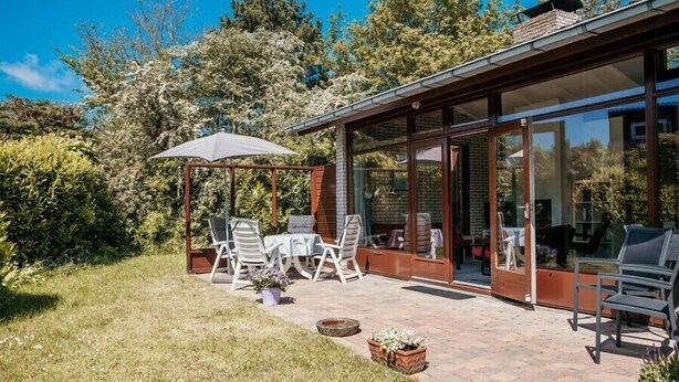 Un patio cubierto con mobiliario exterior, una pérgola y una sala con paredes de vidrio.