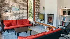 Una sala de estar con pared de ladrillo, un sofá rojo, un sillón negro, un televisor, una chimenea y una estantería.