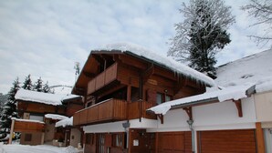 A wooden chalet with a balcony, snow-covered roof, and garage doors.