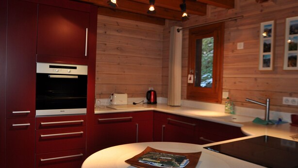 A modern kitchen with wooden cabinets, a built-in oven, a countertop with a toaster, and a window with a view of trees.