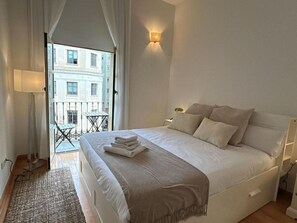 A hotel room with a large bed, a balcony with a table and chairs, and a view of buildings outside.