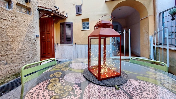 A glass table with a patterned floor, a red lantern, and a door with shutters in a courtyard. - 4bnb - Cozy Vatican Loft With Terrace (Rome)