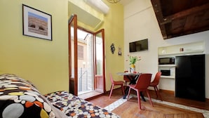 A cozy room with a bed, a dining table with chairs, a kitchen area with a microwave and refrigerator, and a door leading outside. - 4bnb - Cozy Vatican Loft With Terrace (Rome)