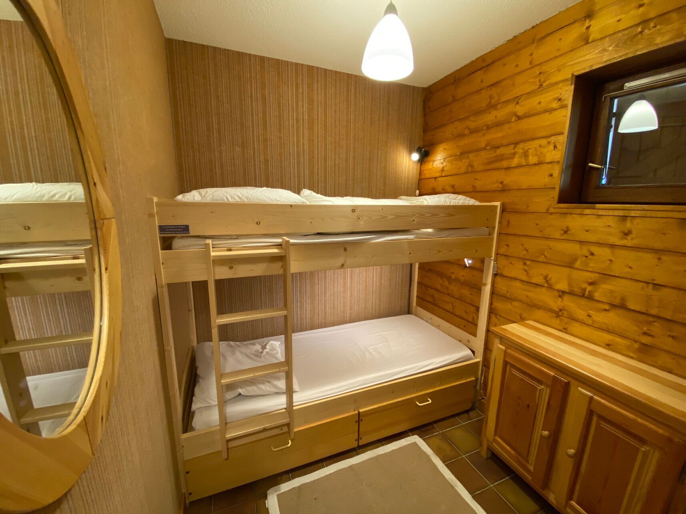 A bunk bed room with wooden walls and a small window.