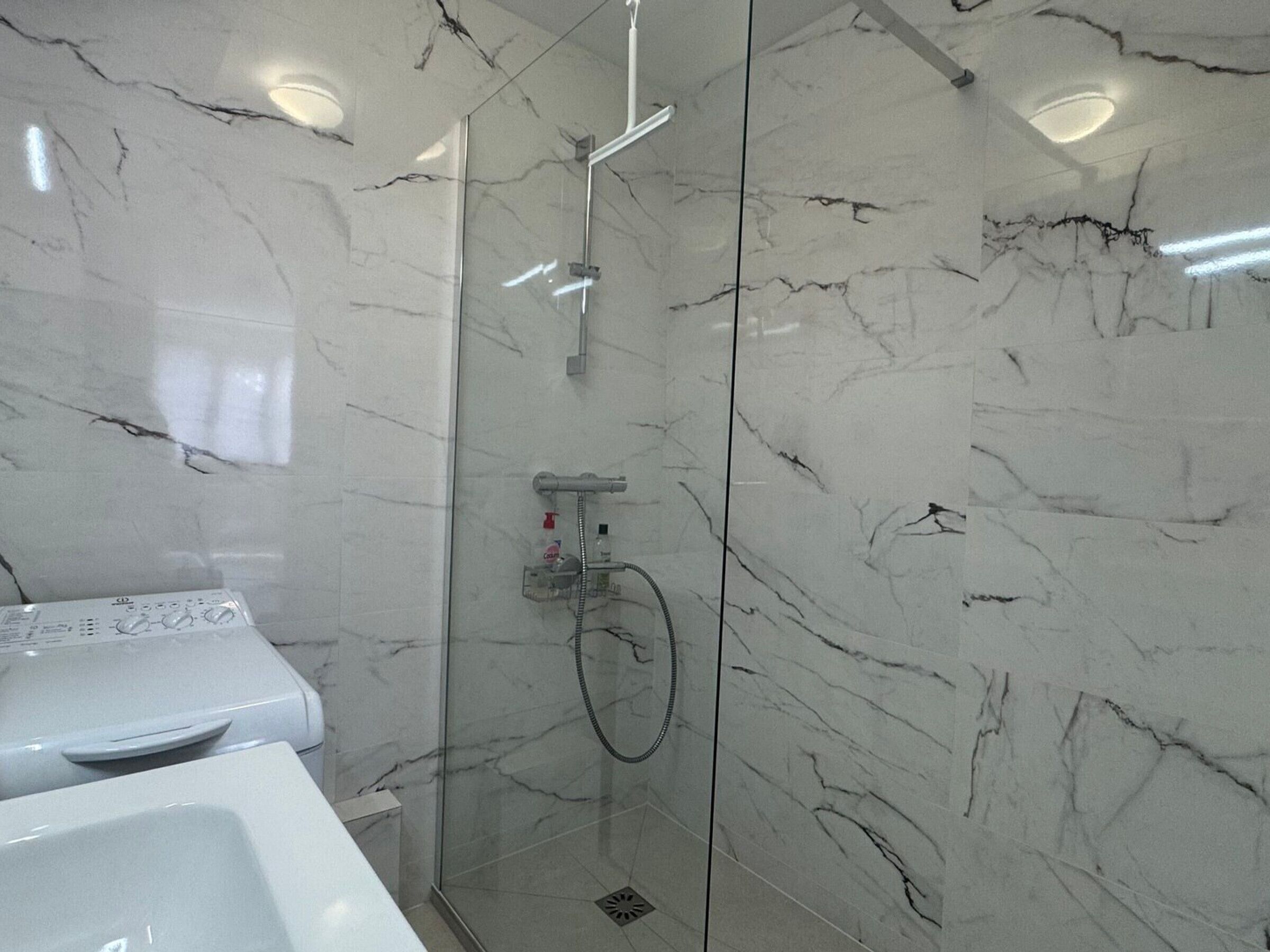 A bathroom with a glass-enclosed shower, marble walls, and a white sink.